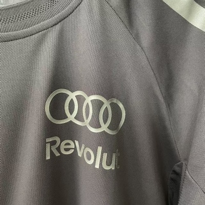 Camisola desportiva cinza com logotipo e texto branco.