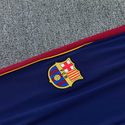 Peça de roupa desportiva azul com emblema FC B e borda vermelha e amarela