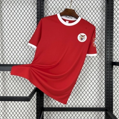 Camisola desportiva vermelha com gola branca e emblemas, pendurada numa estrutura metálica