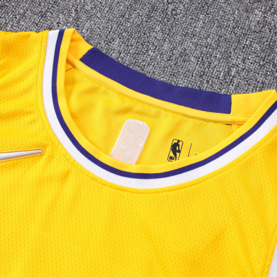 Camisola amarela Nike NBA com detalhes em branco e roxo, tecido perfurado, sobre carpete cinzenta