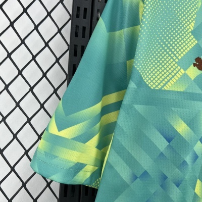 Camisola desportiva verde e amarela com padrão geométrico pendurada num cabide preto perto de parede branca com padrão de grelha