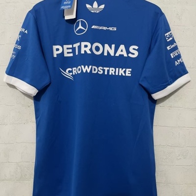 Camisola azul com logótipos brancos PETRONAS e outros pendurada numa parede branca