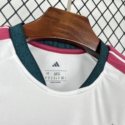 T-shirt desportiva branca Adidas Slim Fit com gola verde escura e detalhes em vermelho pendurada num cabide de madeira.
