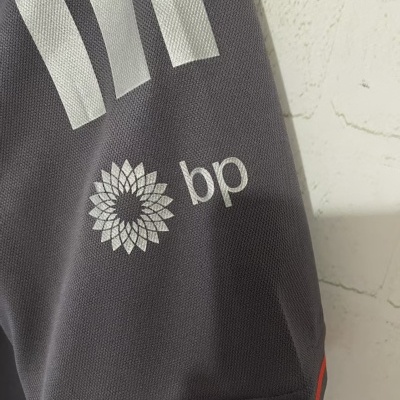 Detalhe de tecido cinza com logótipo bp, riscas brancas e risca vermelha na borda