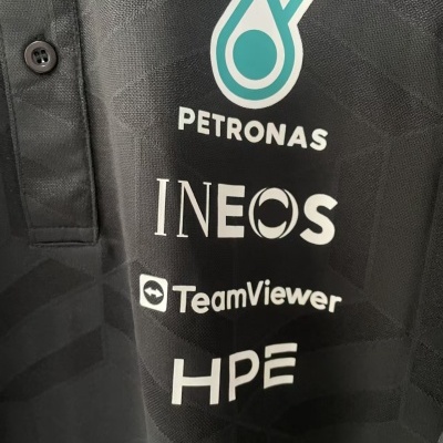 Camiseta polo preta com botões e logótipos PETRONAS, INEOS, TeamViewer e HPE.