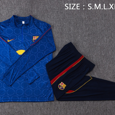 Conjunto de treino azul e calças escuras do FC Barcelona com emblemas do clube e texto de tamanhos numa superfície cinzenta.