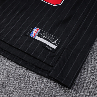 Parte inferior de camisola preta com riscas cinzentas, etiquetas NBA 75 e JORDAN, sobre chão cinzento.