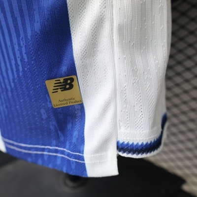 Detalhe de camisola azul e branca com etiqueta dourada NB