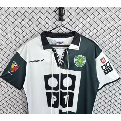 Camisola de futebol Sporting Portugal Reebok com gola e cordões, em verde e branco, pendurada numa rede preta.