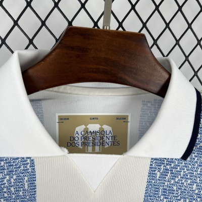 Camisola branca com padrão azul e etiqueta com texto em fundo bege pendurada em cabide de madeira