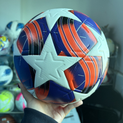 Bola de futebol branca com estrelas, detalhes azuis e vermelhos, segurada por mão
