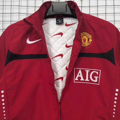 Casaco desportivo vermelho com emblema do Manchester United e logotipos Nike e AIG em fundo branco