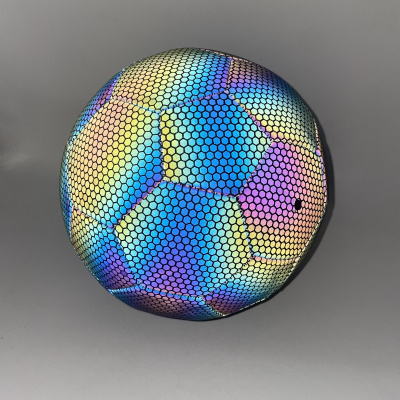 Bola colorida com padrão hexagonal iridescente colocada sobre superfície cinzenta.
