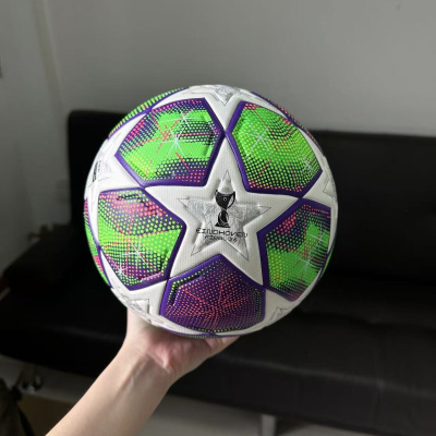 Bola de futebol colorida com padrão de estrelas, segurada por mão em ambiente interno