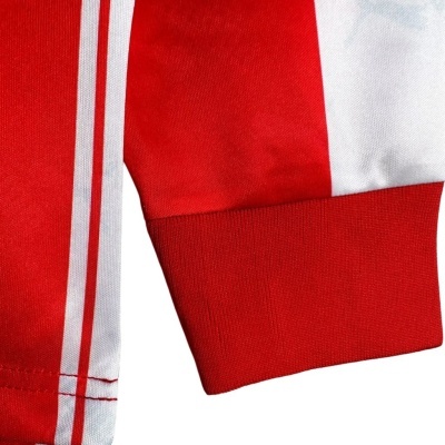 Manga vermelha e branca com punho elástico vermelho e duas faixas brancas verticais.