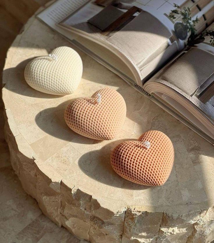Vela Aromática Coração Três corações decorativos em malha sobre mesa de pedra com livro aberto ao fundo