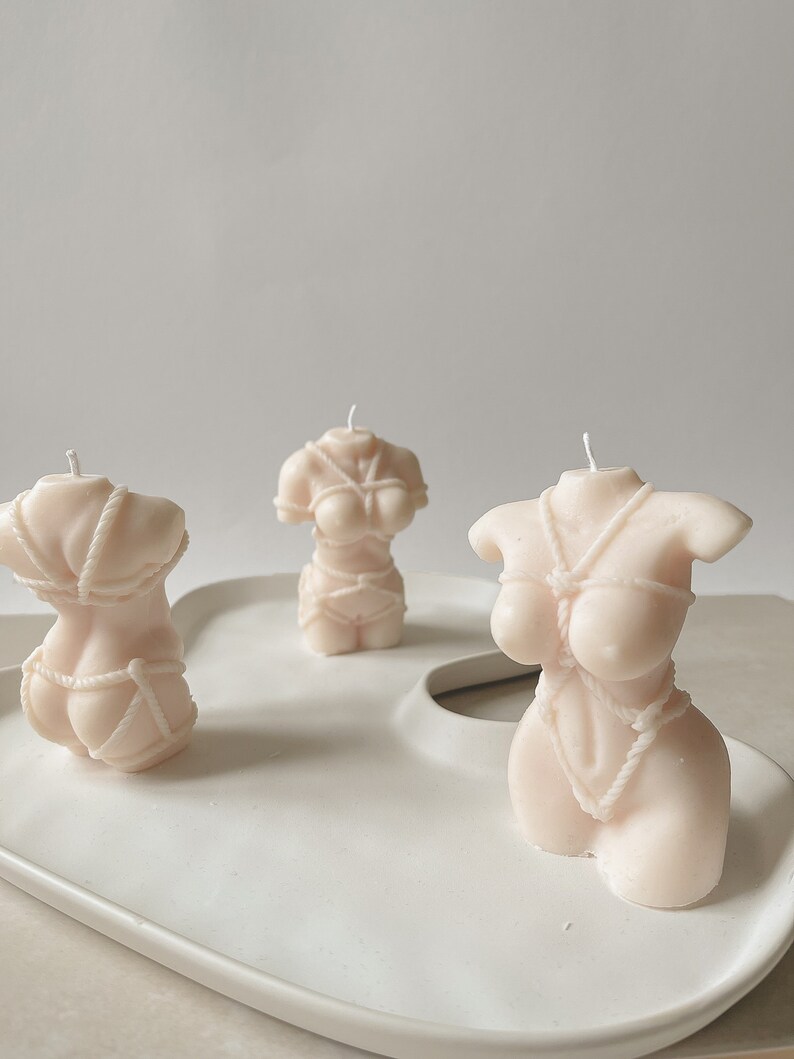 Trio de Velas Aromáticas Corpo Feminino Velas creme em forma de tronco feminino com lingerie sobre prato branco.