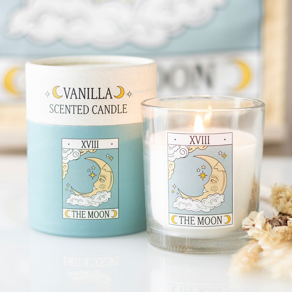 Vela perfumada de baunilha com ilustração de lua em embalagem azul e branca e vela acesa num copo de vidro com o mesmo desenho.