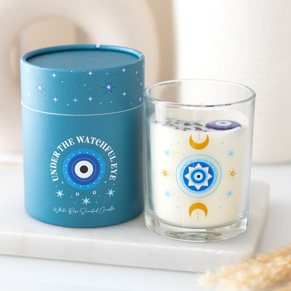 Vela perfumada branca em vidro decorado ao lado de embalagem cilíndrica azul com texto e estrelas