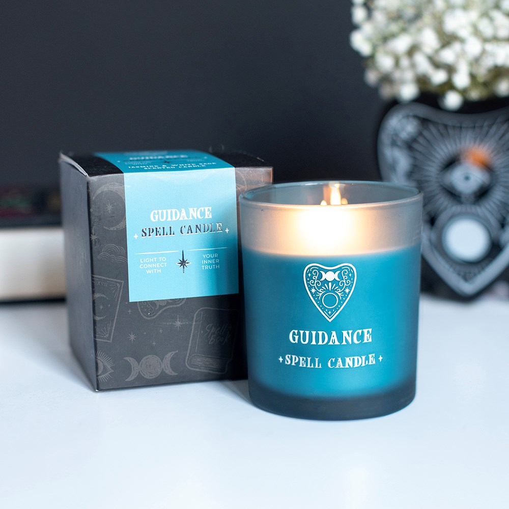 Vela Guidance Spell Candle azul acesa com embalagem preta e azul ao lado em superfície branca