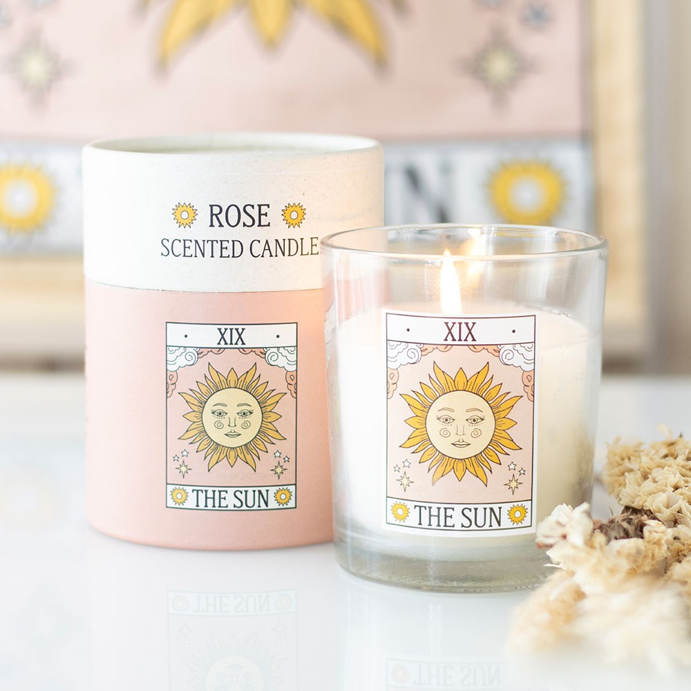 Vela aromática em copo de vidro com etiqueta sol e embalagem cilíndrica rosa e branca