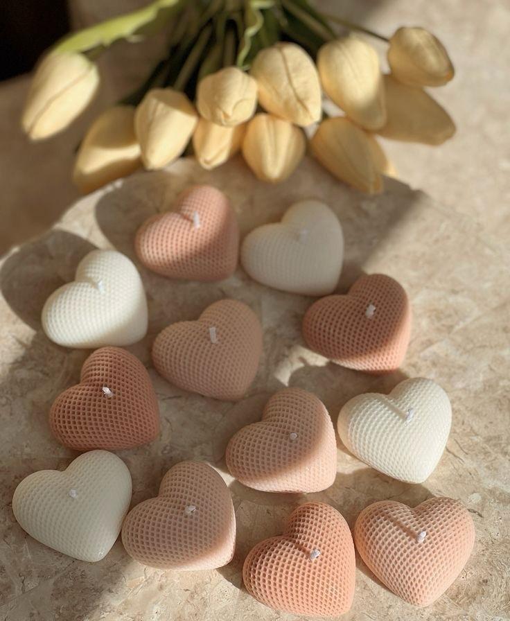 Vela Aromática Coração Velas em formato de coração com textura canelada em cores suaves sobre pedra clara com flores artificiais bege