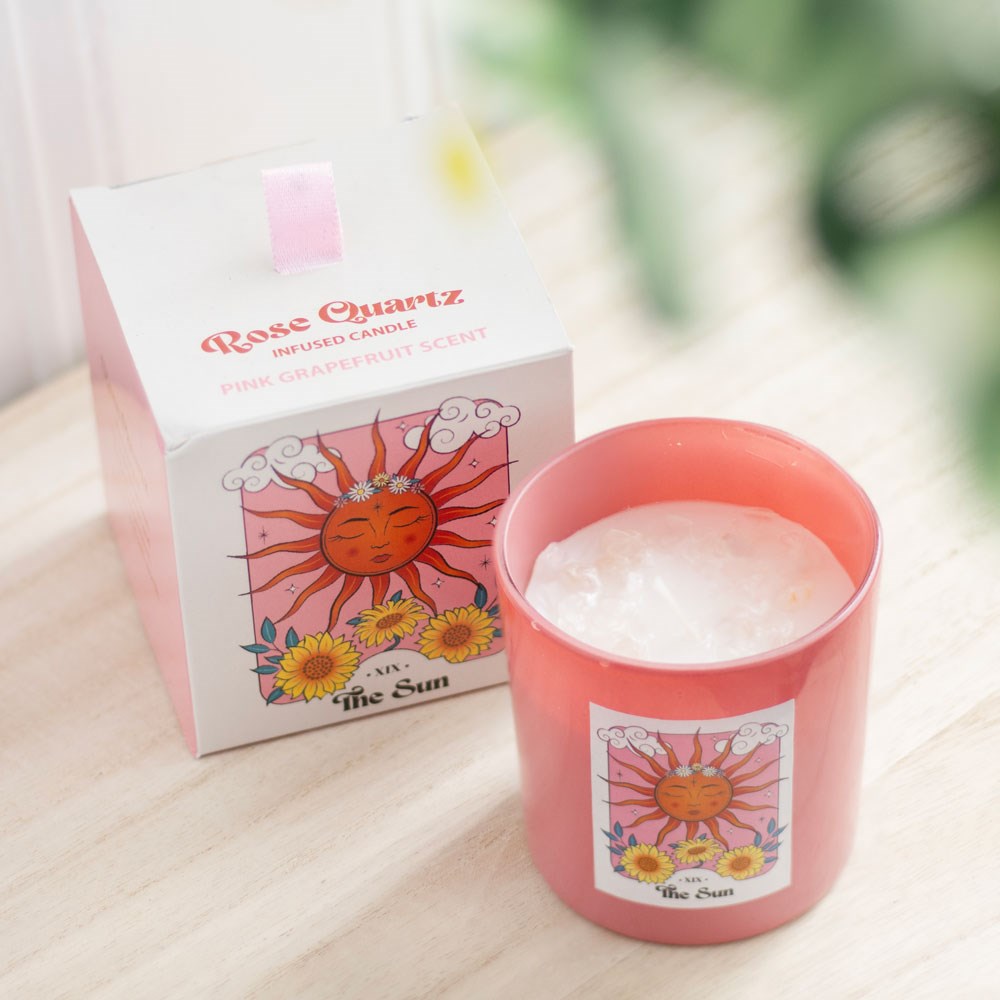 Vela Rose Quartz num copo rosa com etiqueta do sol e flores, e caixa correspondente ao lado