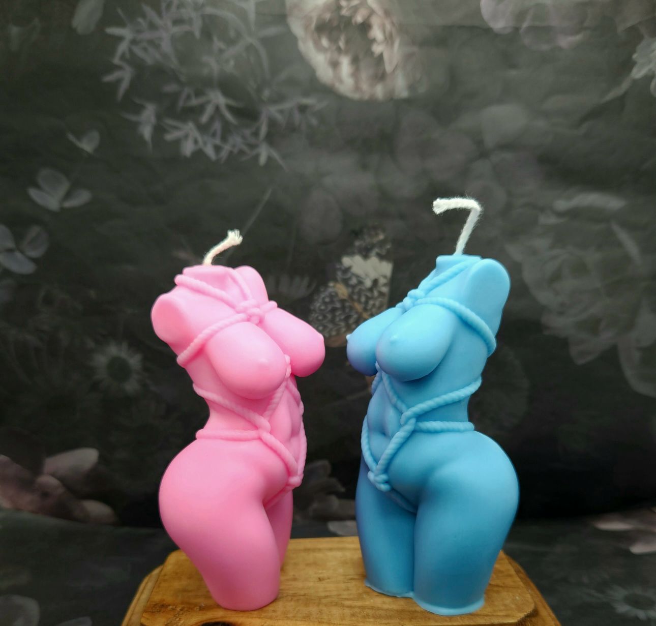 Vela Aromática Corpo Feminino Velas decorativas em forma de corpo feminino cor-de-rosa e azul com cordas, sobre base de madeira.