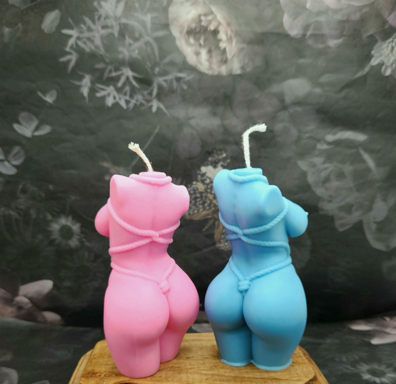 Vela Aromática Corpo Feminino Duas velas corpóreas rosa e azul sobre superfície de madeira com fundo cinzento desfocado