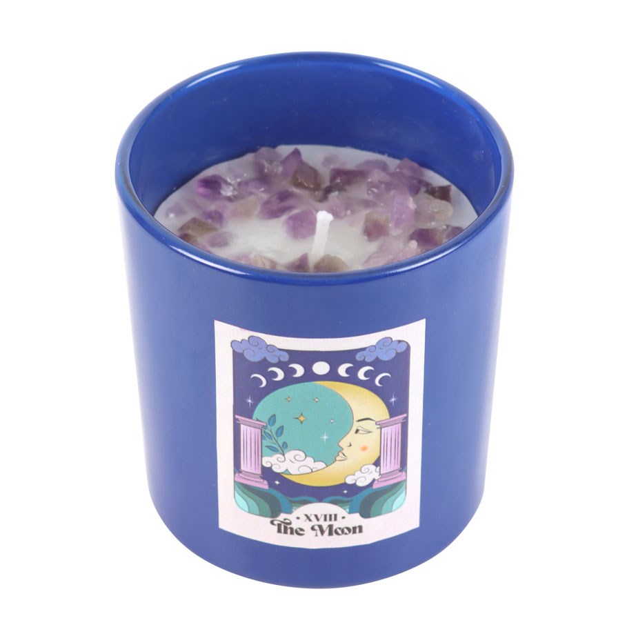 Vela branca em suporte azul com pedras roxas e etiqueta com lua.