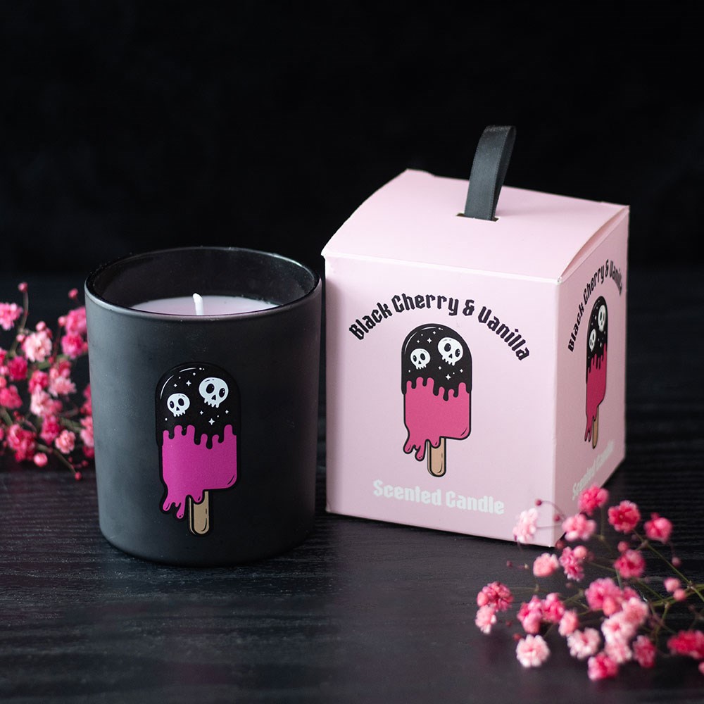 Vela numa jarra preta ao lado de caixa rosa com design de gelado e texto sobre aroma