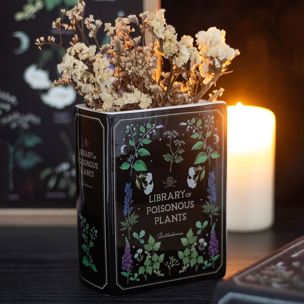Vaso preto decorado com plantas e texto, com flores secas e vela acesa ao fundo