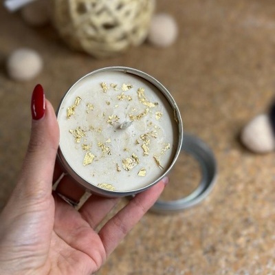 Vela branca com decoração dourada num recipiente metálico prateado