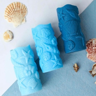 Três velas azuis com relevo de conchas e estrelas-do-mar em superfície branca e azul com conchas naturais