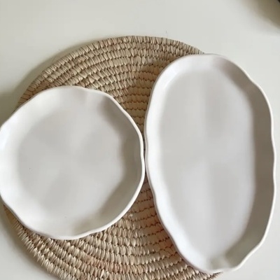 Dois pratos brancos em cerâmica com bordas onduladas sobre um descanso de mesa de rattan.