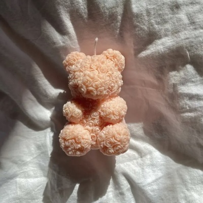 Vela em forma de urso feita de flores pequenas pêssego sobre tecido branco