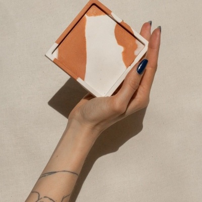 Mão com unha azul a segurar prato quadrado de cerâmica marmoreado branco e terracota