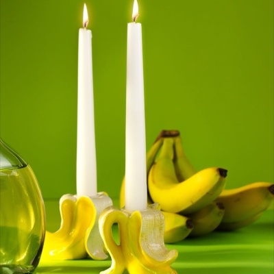 Dois castiçais em forma de banana com velas acesas e bananas atrás, sobre fundo verde