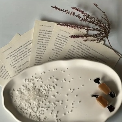 Prato oval branco com sal grosso, caramelos e páginas de livro em fundo branco