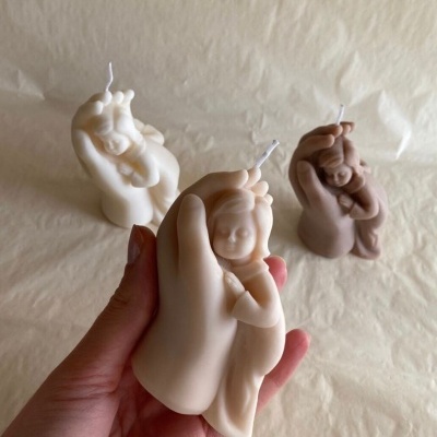Três velas em forma de mão segurando figura de bebé em tons neutros