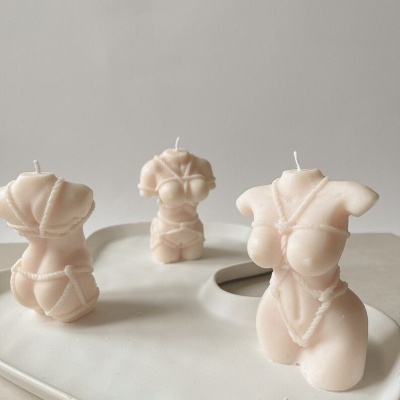 Velas creme em forma de tronco feminino com lingerie sobre prato branco.