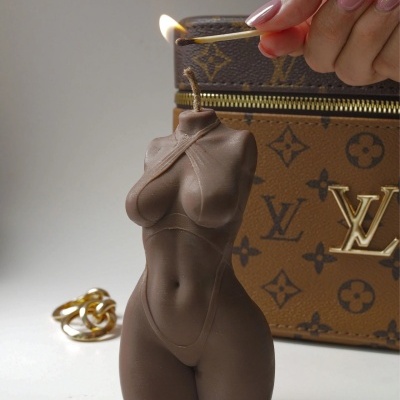 Vela decorativa em forma de torso feminino castanho junto a mala e anel