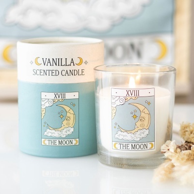 Vela perfumada de baunilha com ilustração de lua em embalagem azul e branca e vela acesa num copo de vidro com o mesmo desenho.