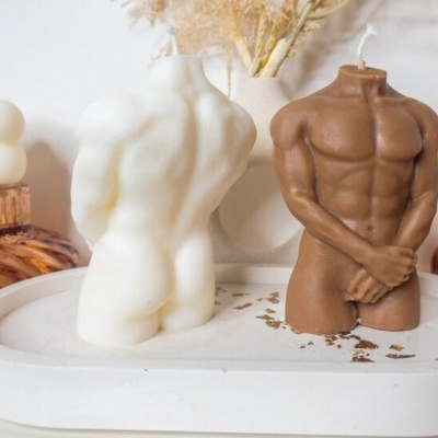 Velas decorativas em formato de torso masculino em base branca com vasos ao fundo