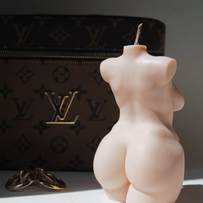 Vela em forma de torso humano bege com bolsa Louis Vuitton e dois anéis dourados ao fundo
