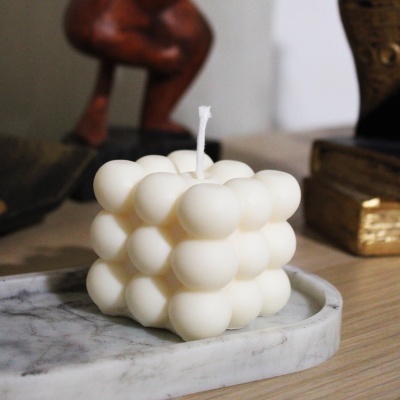 Vela branca em forma de cubo com bolhas sobre base de mármore