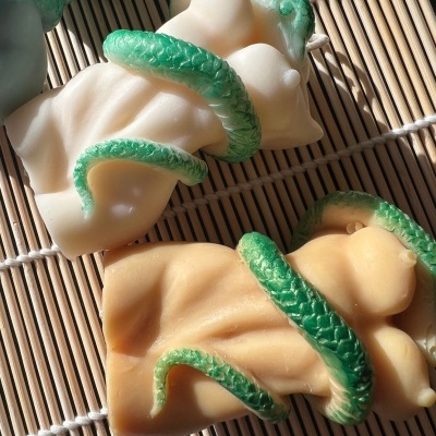 Velas decorativas em forma de corpo feminino com cobra verde enrolada sobre esteira de bambu