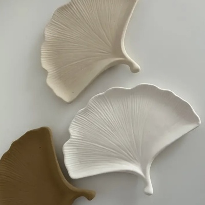 Três pratos decorativos em forma de folha com textura e cores bege, branco e castanho