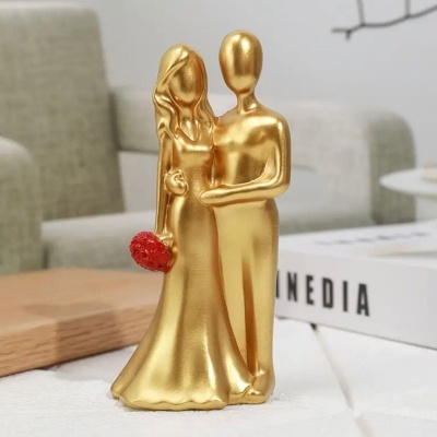 Estatueta dourada de casal estilizado com ramo vermelho