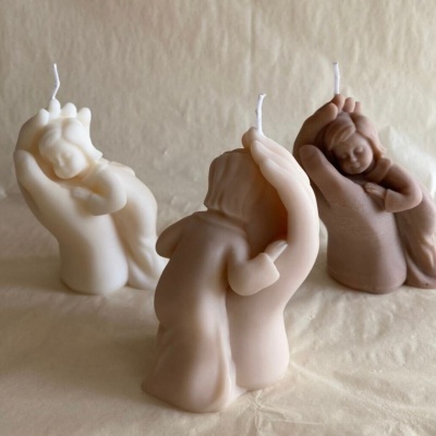 Velas em forma de mãos segurando bebés em tons bege e castanho